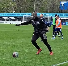 A coach wearing goalkeeper gloves kicks the ball