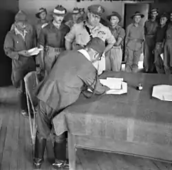 Masao Baba, Lieutenant General of the Japanese 37th Army signs the surrender document in Labuan, British Borneo, being watched by Australian Major General George Wootten and other Australian units.