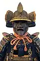 The fukigaeshi can be seen to both sides of the mabizashi (brim), and the shinobi-no-o (cord) secures the mengu (facial armour).