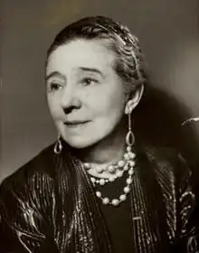 Shoulder height portrait of middle-aged woman with her hair up, wearing a black leather jacket, necklace and long earrings