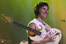 A man wearing a sleeveless white shirt holding a white guitar