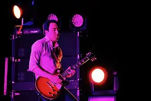 Jeff Schroeder backlit in pink, playing guitar onstage