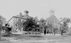 Two buildings surrounded by trees, with the left building sporting a front deck area and topped with a cupola, and the right one presenting a flat front face and a small tower on the top