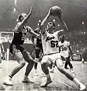 Sloan readying to jump with the basketball in his hand and a defender between him and the net