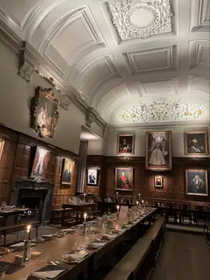 A wood-panelled hall, with a large portrait of Elizabeth I in the middle of the far wall; other portraits alongside and around the walls; a white plaster ceiling with light blue decoration