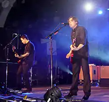 Two men performing onstage playing and singing into a microphone