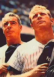 "Two men in New York Yankee pinstrips stand attention with Yankee caps over their heart."