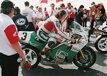 Rider seated without helmet on white and green motorcycle prior to race