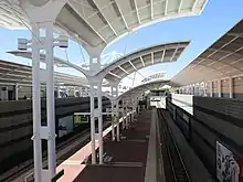 Island platform in a trench surrounded by retaining walls. There are large curved white shelters covering the platform.