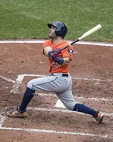 A man in an orange baseball uniform and dark blue batting helmet swings his bat.