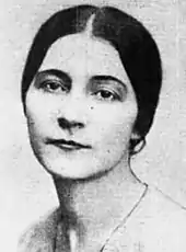 Black and white portrait of a woman with her hair parted in the middle and in a bun, dressed in a light-colored v-necked blouse