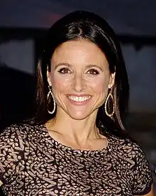 A woman with black hair tied in a knot wearing a black dress, at a crowded event.