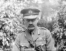 Julian Byng in a black and white chest high portrait with foliage behind him. Byng has a moustache and is wearing a general officer's uniform that consists of a tailored jacket adorned with brass buttons. The collar is embellished with additional decorations denoting rank and service branch. He is wearing a peaked cap featuring ornate insignia indicating his rank and unit affiliation.