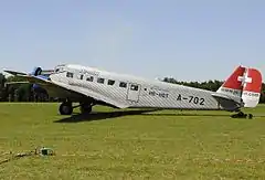 A silver transport aircraft with the Swiss cross painted on its tail on a grassy airfield