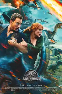 A man and a woman take cover behind a spherical vehicle, while various dinosaurs run from an erupting volcano.