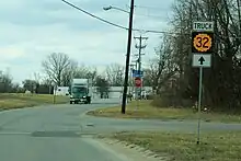 A two-lane road in a developed but semi-rural area. A sign advises trucks to continue straight for K-32 Truck.