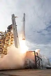 Fire erupts from the rockets engine as smoky rocket exhaust bounces off of the launch pad and smoky vapors trail down the side of the vehicle