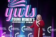 Kat Cammack addressing the Young Women's Leadership Summit 2022 in Grapevine,  Texas. She's wearing a red dress and is talking into a microphone.