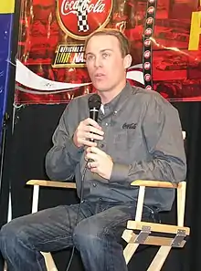 A man at a press conference wearing a gray shirt and holding a microphone in both his hands