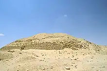 Ruined pyramid raising a few metres from the desert floor, a heap of sand and mudbricks.