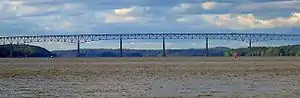 Panorama of a bridge over a wide river with mountains visible in the distance.