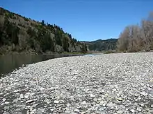 A big patch of bright-colored stones beside the shallow-looking river