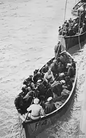 Photograph looking down on two lifeboats crammed with people in naval uniforms. A third lifeboat of a different design can be seen behind the first two.