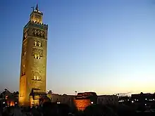 A ground view of an artificially lit tower, reaching several storeys high, at the beginning of a sunset.