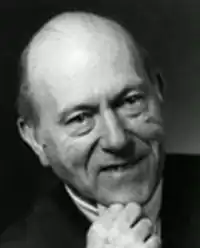 Clean-shaven, half-smiling man with receding hair, leaning slightly to one side, stroking his chin.