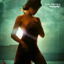 Minogue covers her body with a dark red towel, while facing to the right. She is standing in front of a window blind, with a light can be seen filtering through.