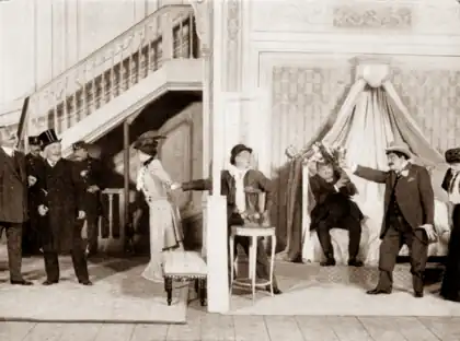 stage scene with characters in early 20th-century dress in scene of frantic confusion