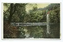 A calm lake with refelctions in the water, to the right is Stone Tower studio behind trees