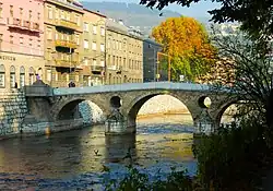 Latin bridge (prev. Princip bridge) in Sarajevo. Across the bridge is a street of several grayish houses not more than four stories high.