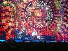 Robert Plant singing and Jimmy Page playing guitar in front of a large screen displaying an elaborate design.