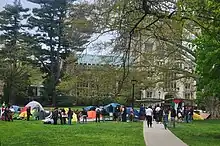  tents, signs, and people standing on green grass in front of the Vassar College Library