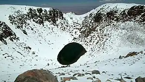 Aerial view of Licancabur Lake, surrounded by a snow-covered inwards-sloping crater