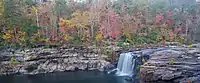 A waterfall flows over rocks by a forest in fall colors