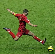 Gerrard wearing an all-red kit and powerfully kicking a yellow ball in a match