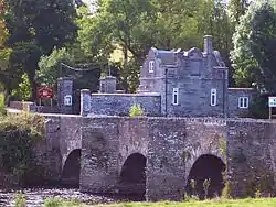 stone gatehouse and gateway seen beyond three arches of old bridge over river