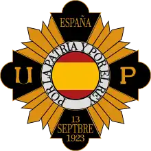 The yellow and black emblem of the Unión Patriótica. The Spanish flag is in the middle of the emblem, contained in a circle shape.