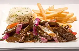 Lomo saltado with onions, tomatoes, french fries and white rice.