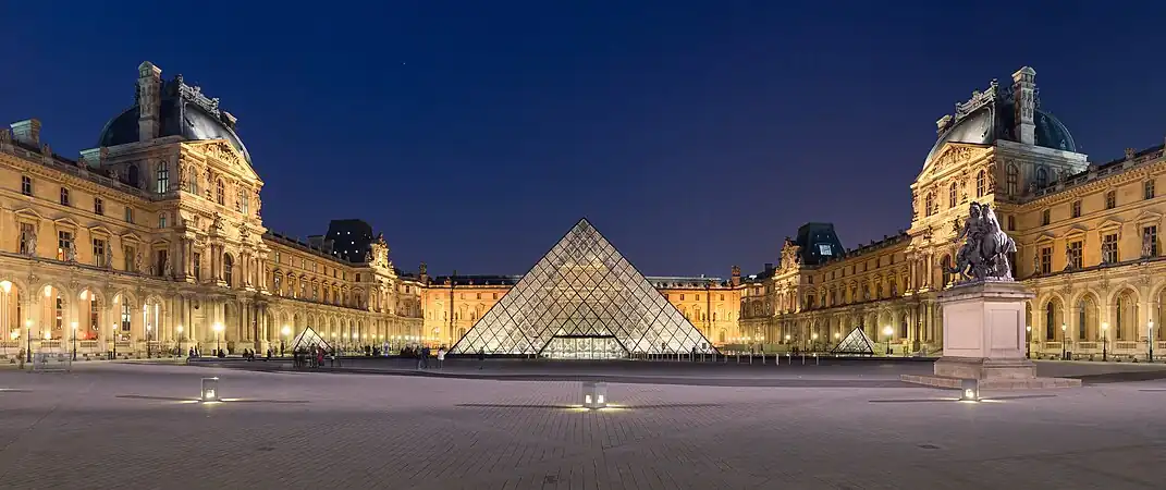 Nighttime scene of the Louvre courtyard in Paris, with the iconic glass pyramid designed by I.M. Pei in the foreground and the palace in the background