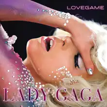 Gaga places her left hand on her forehead and tilts it backwards. The arm is painted in blue and violet colors and glitters are pasted on it.