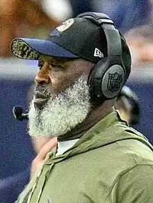 Photograph of Smith wearing a Texans sweatshirt, Texans baseball cap and headset on the Texans sideline