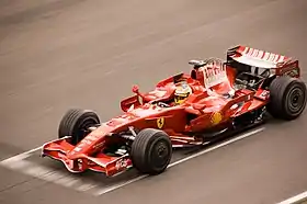 a red open wheeled racing car travels at speed down a tarmac course