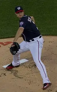 A man in a dark blue baseball jersey with a curly "W" on his cap throws a pitch.