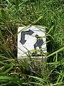 Carving of a man resting with hands on knees on a square stone marker in grass