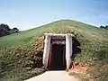 Front view of earth lodge, showing timber doorway into grassy mound