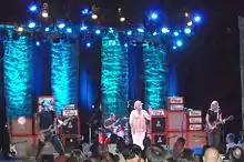 Magnapop perform onstage in front of a blue backdrop and several stacks of Orange amplifiers