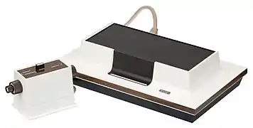 Photograph of a dedicated video game console with two input devices connected to it with cables.